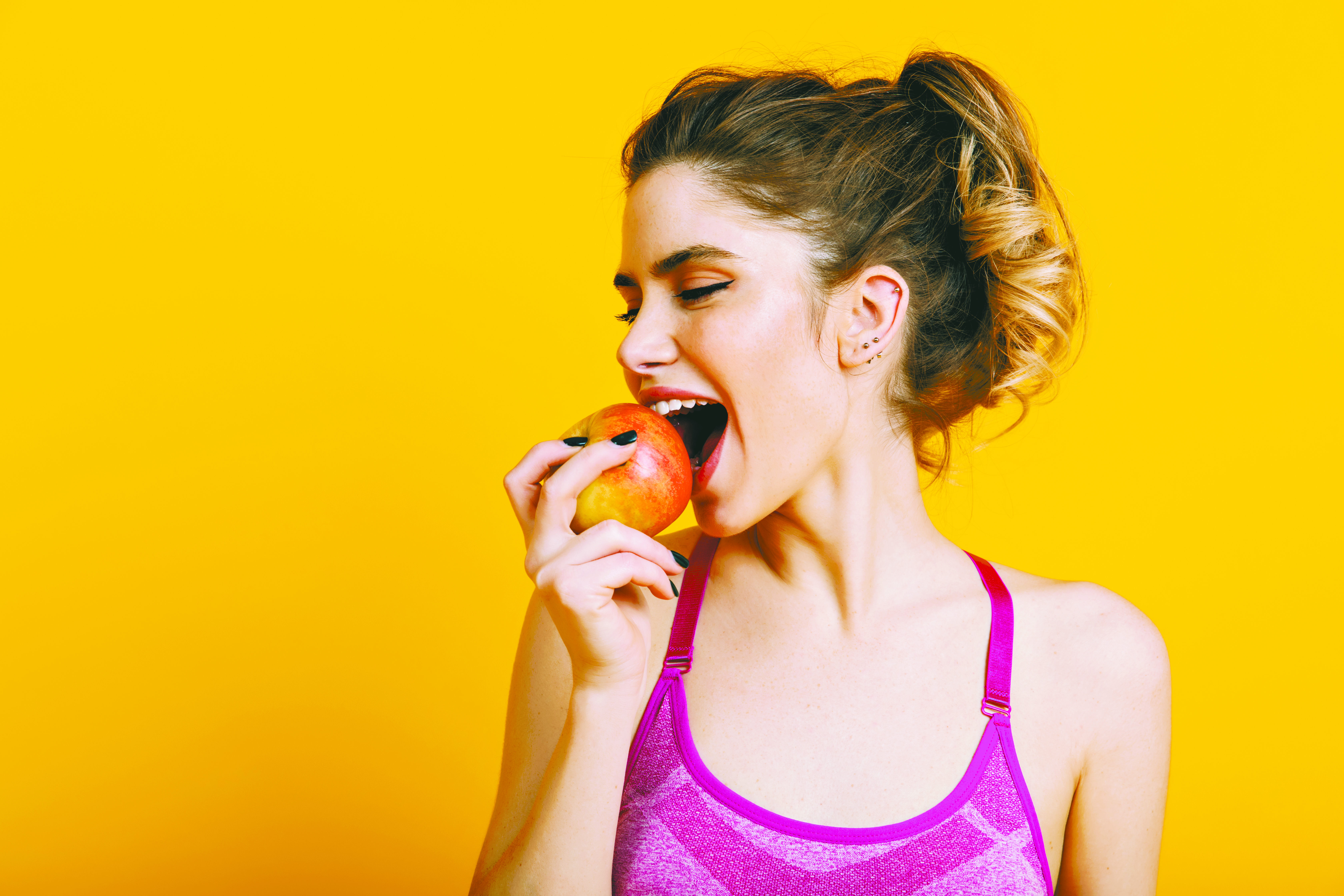 Indoor photo of blissful woman eating apple. Brunette fitness girl enjoying fruits